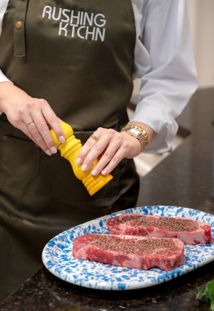 Chef Alex Rushing seasoning steaks in a Rushing KTCHN apron